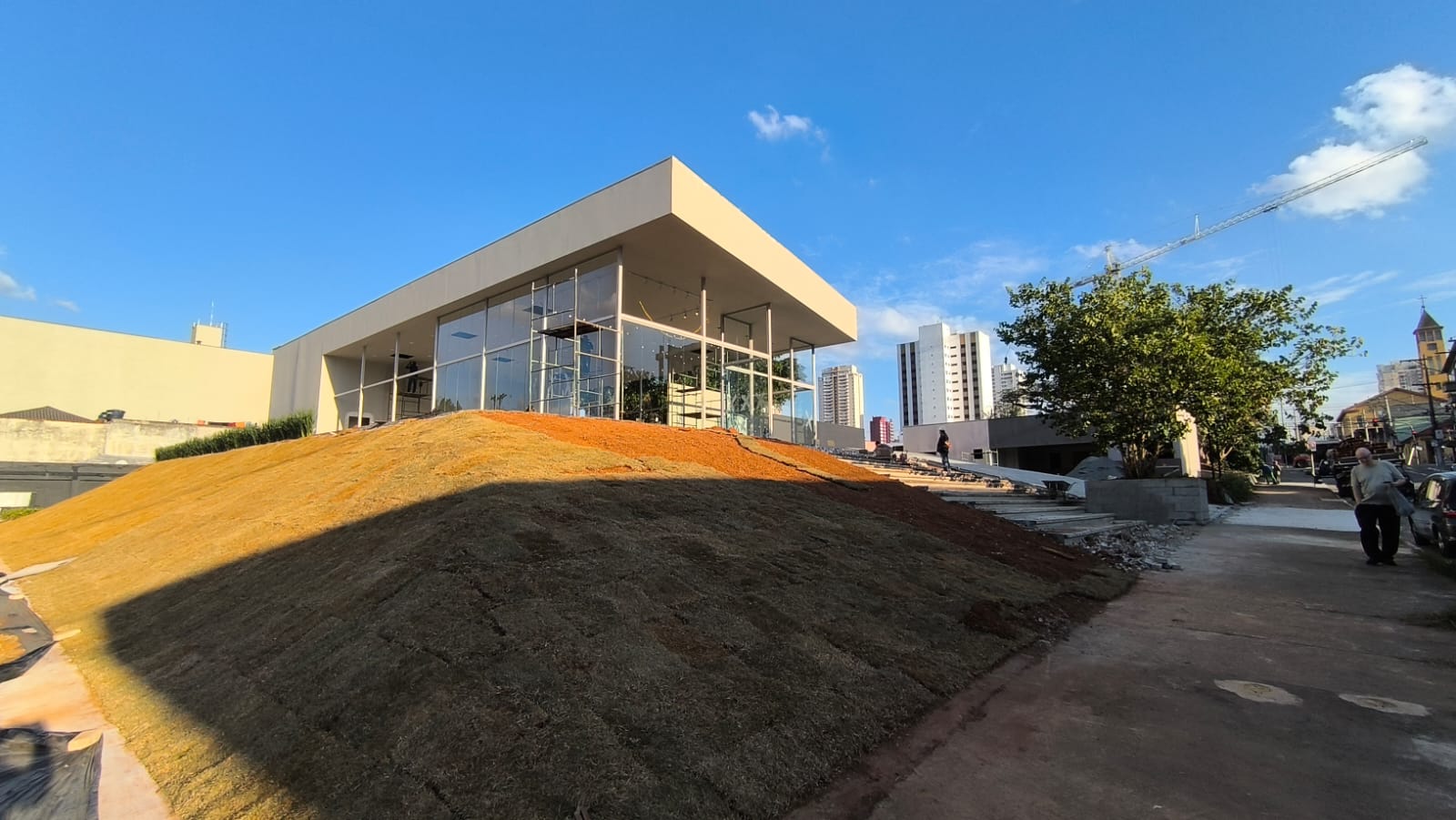 Fachada do stand de vendas do Orbya Vila Carrão quase pronto: pavilhão de vidro com cobertura plana e paisagismo em finalização na Vila Carrão